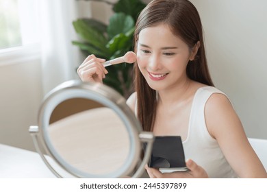 Skin care beauty, applying make up concept, smile asian young woman, cute girl make up on face by brush blush powder on her cheek, looking at the mirror. Lady with cosmetic with fashion lifestyle