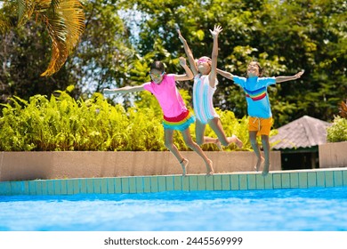 一群孩子跳进游泳池。夏日水上乐趣。孩子们在室外游泳池玩耍。带小孩的夏季家庭度假。在热带度假村度假。带孩子旅行。