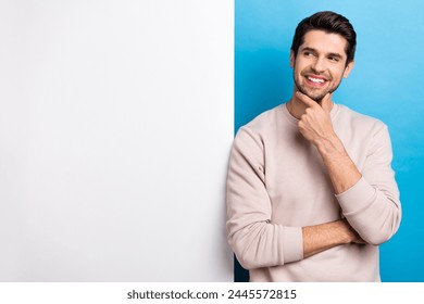 Photo of nice young man think look empty space placard wear beige sweatshirt isolated on blue color background
