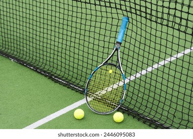 Raket tenis dan bola tenis di samping net di lapangan tenis luar ruangan.