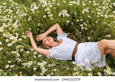 Uma mulher está deitada em um campo de camomila, vestida com um vestido branco