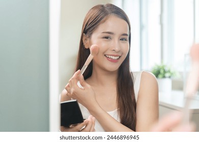 Skin care beauty, applying make up concept, smile asian young woman, cute girl make up on face by brush blush powder on her cheek, looking at the mirror. Lady with cosmetic with fashion lifestyle