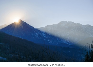 Soarele de iarnă în spatele unui vârf de munte al unui peisaj alpin de iarnă la Barcis, Friuli-Venezia Giulia, Italia