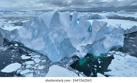 Flying over giant iceberg near Ilulissat, Greenland. Iceberg pieces break off and fall into the water. Aerial arctic nature landscape, global warming and climate change concept