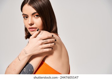 Een jonge vrouw met bruin haar toont een tatoeage op haar arm in een studio.