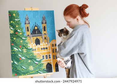kız sanatçı resmini inceliyor ve kollarında bir kedi tutuyor