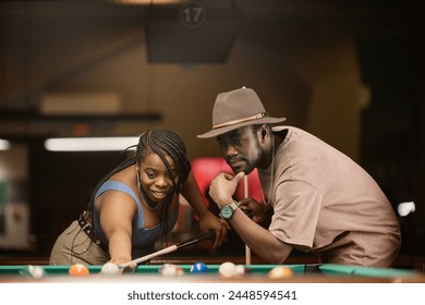 Portrait vun erwuessener afroamerikanesch Koppel déi Pool zesumme spillen a sech iwwer den Dësch am Nuetsclub lenken