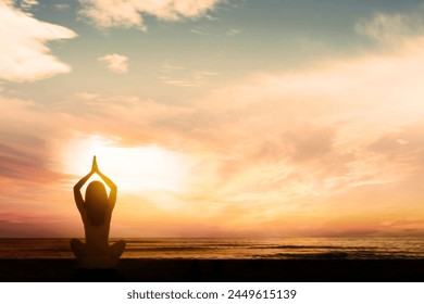 Silhouette of young woman exercising yoga while doing meditation at beach during sunrise or sunset