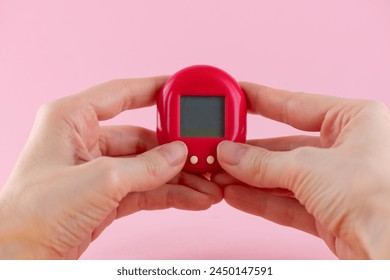Mascota virtual del juego Tamagotchi en manos sobre un fondo rosa.