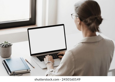 Woman working in office, using laptop computer with blank white screen display mockup