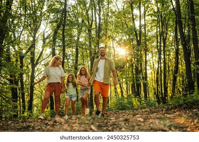 Portrait of a explorer family holding hands and taking a walk in nature. A young adventurous family is taking a walk in forest and exploring nature. Family holding hands and strolling in nature.