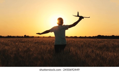 Ragazzo adolescente allegro che corre con un aeroplano giocattolo su un campo di grano autunnale al tramonto cinematografico, vista posteriore da vicino. Bambino maschio attivo che gioca con un aeroplano giocattolo che vola, si gode la libertà, un'infanzia felice nel prato.