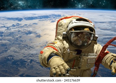 A cosmonaut floats in space above Earth. Stars shine in the background. Elements of this image furnished by NASA.