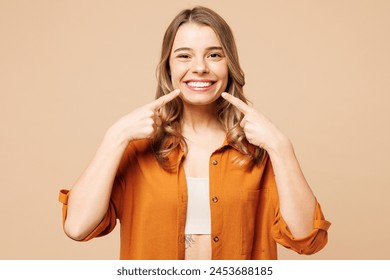 Young smiling happy Caucasian woman she wear orange shirt casual clothes point index fingers on opened mouth teeth isolated on plain pastel light beige background studio portrait. Lifestyle concept