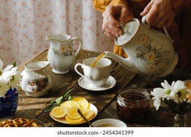 Przyjęcie herbaciane, poranne śniadanie. Nalewanie herbaty z czajnika do porcelanowej filiżanki w rustykalnej kuchni.