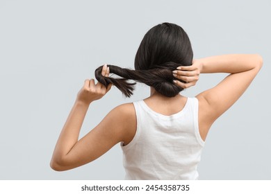 Người phụ nữ trẻ đẹp với mái tóc dài khỏe mạnh trên nền xám, nhìn từ phía sau