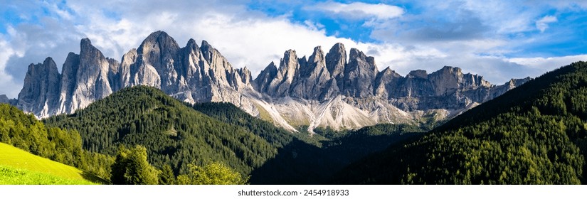 義大利多洛米蒂山脈鋸齒狀的山峰，其岩石表面與山腳下鬱鬱蔥蔥的綠色森林以及上面飄著蓬鬆雲彩的清澈藍天形成鮮明對比。