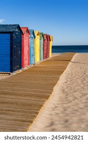 Farbige Kabinen und Hütten an einem Strand mit Sand, Holzweg unter blauem Himmel