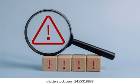 A magnifying glass is placed on top of a stack of wooden blocks with red exclamation points on them. Concept of urgency and danger, as the red exclamation points