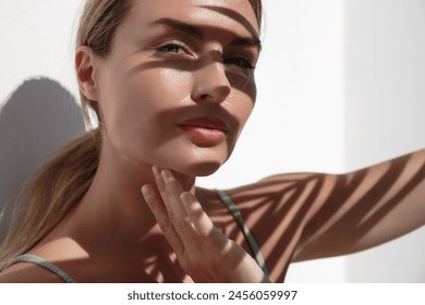 흰 벽에 야자수 잎의 그림자가 드리워진 젊은 여성.