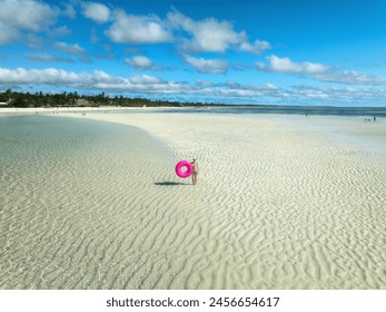 Aerial view of sporty slim woman with swimming ring, sandy beach, blue sea during low tide at sunny summer day in Zanzibar island. Top view of beautiful girl, sandbank, ocean, sky with clouds, palms