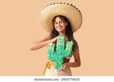 Schéin jonk afrikanesch-amerikanesch Fra am Sombrero Hut mat Pinata a Form vu Kaktus op brongen Hannergrond