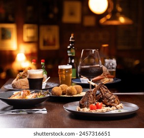 Abendessen in einem Steakhouse mit Lammkarree mit Kartoffelpüree und Kirschtomaten und einem Glas Rotwein und Craft-Bier und unscharfem Pub-Hintergrund