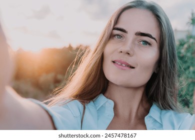 Amber Golden Hour Krupni plan žene okupane u zlatnočasovnom svjetlu koja pravi selfi na zalasku sunca u ljetnom parku. Sretni turist uživa u snimanju selfija na otvorenom za uspomene