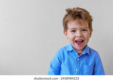 Anak laki-laki kecil yang tersenyum lucu mengenakan kemeja melihat kamera pada latar belakang abu-abu, ruang copy