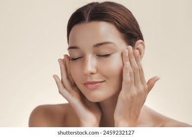 Cosmetics skincare concept photo. Woman with beautiful face touching healthy facial skin portrait. Beautiful smiling Asian girl model with natural makeup enjoys glowing hydrated smooth skin on beige