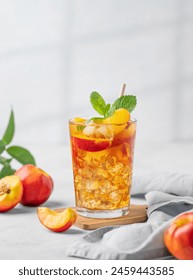 Thé glacé à la pêche et à la menthe rafraîchissant. Concept d'une boisson estivale fraîche et saine, faite maison, servie dans un grand verre sur un fond clair avec des fruits frais et des ombres. Vue de face et espace pour le texte.