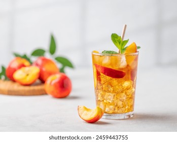 Thé glacé à la pêche et à la menthe rafraîchissant. Concept d'une boisson estivale fraîche et saine, faite maison, servie dans un grand verre sur un fond clair avec des fruits frais et des jeux d'ombres. Vue de face.
