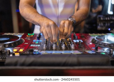 Bir DJ'in ellerinin canlı performans sırasında aydınlatılmış düğmelere ve kaydırıcılara odaklanarak müzik mikserinin kontrollerini ustalıkla kullandığı yakın çekim görüntüsü.