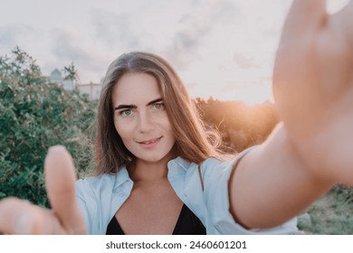 Amber Golden Hour Krupni plan žene okupane u zlatnočasovnom svjetlu koja pravi selfi na zalasku sunca u ljetnom parku. Sretni turist uživa u snimanju selfija na otvorenom za uspomene