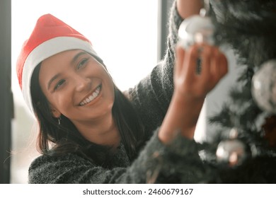 Woman, decorating and Christmas tree in home for holiday with smile, peace with relax for party. Female person, happiness and celebrate on vacation with festive joy, hanging ornament for winter break
