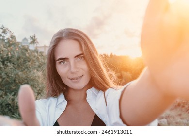 Amber Golden Hour Krupni plan žene okupane u zlatnočasovnom svjetlu koja pravi selfi na zalasku sunca u ljetnom parku. Sretni turist uživa u snimanju selfija na otvorenom za uspomene