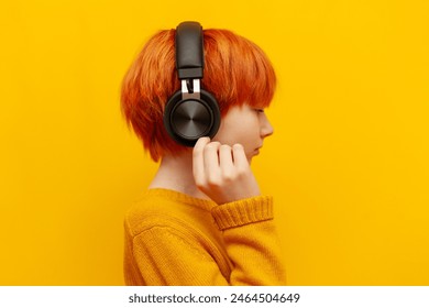Cậu bé tóc đỏ đeo tai nghe đen đang nghe nhạc trên nền màu vàng tách biệt, một thiếu niên tóc cam đeo tai nghe