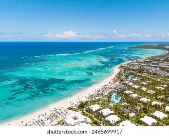 Pemandangan udara pantai berpasir putih dengan banyak hotel all inclusive di Punta Cana. Air berwarna biru kehijauan, pohon palem yang tinggi, dan payung jerami di pantai. Tempat terbaik untuk liburan musim panas