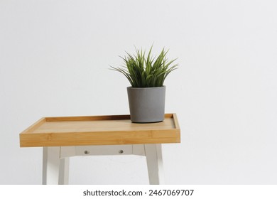 Un jarrón de flores gris con flores verdes sobre una mesa de madera cuadrada con un color marrón y un fondo blanco puro.