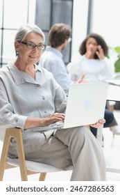 zrela žena sjedi s laptopom i gleda u kameru