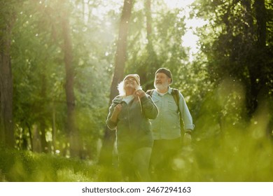 Senior couple, man and woman taking peaceful walk in park, enjoying tranquility and the beauty of nature. Sunlight and greenery. Concept of sport, aging, active and healthy lifestyle, health care