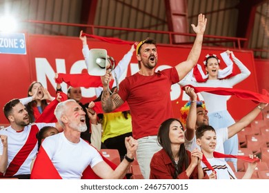 Sport fans are cheering for their team at the stadium on the match. The cheer leader uses a megaphone