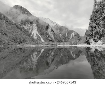 Această fotografie surprinde munți și un lac sub un cer gri, prezentând un peisaj sumbru, dar frumos.