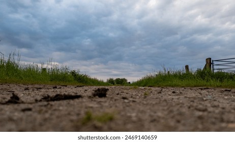 Laag standpunt van een grindweg door weilanden, vastgelegd onder een bewolkte hemel op een lenteavond.