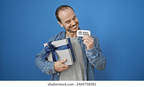 A smiling man holding a gift and a gift card against a blue background.