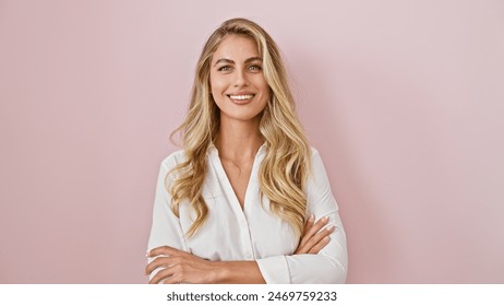 Jeune femme blonde joyeuse debout avec confiance, les bras croisés, exprimant sa joie et son bonheur sur un fond rose isolé !