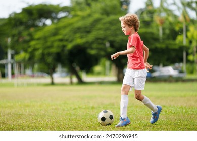 Anak bermain sepak bola. Anak-anak bermain sepak bola di lapangan terbuka. Anak laki-laki kecil menendang bola di taman musim panas. Aktivitas sehat untuk anak-anak kecil. Tim klub olahraga sekolah. Liga sepak bola junior.