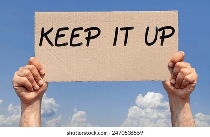 Ruce držící kus kartonu s nápisem "keep it up"