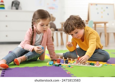 Fëmijë të vegjël të lezetshëm që luajnë me lojën matematikore "Peshkimi i numrave" në dyshekun e enigmës në kopshtin e fëmijëve