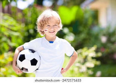 Fanul fotbalului Angliei aplaudă. Copiii joacă fotbal și sărbătoresc victoria pe teren în aer liber. Suporterul echipei Angliei. Băiețel în tricou englezesc și crampoane lovind mingea. Antrenament sportiv pentru copii.